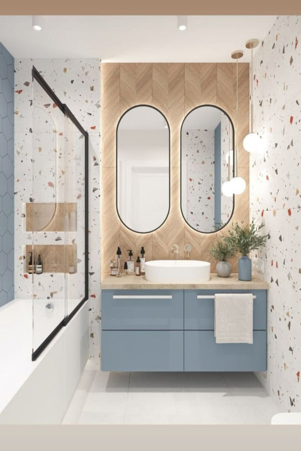 Modern bathroom with blue vanity, double mirrors, and decorative elements. It has a colorful terrazo tile on walls