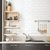 Modern kitchen with white tiled wall, wooden shelves, and hanging utensils.